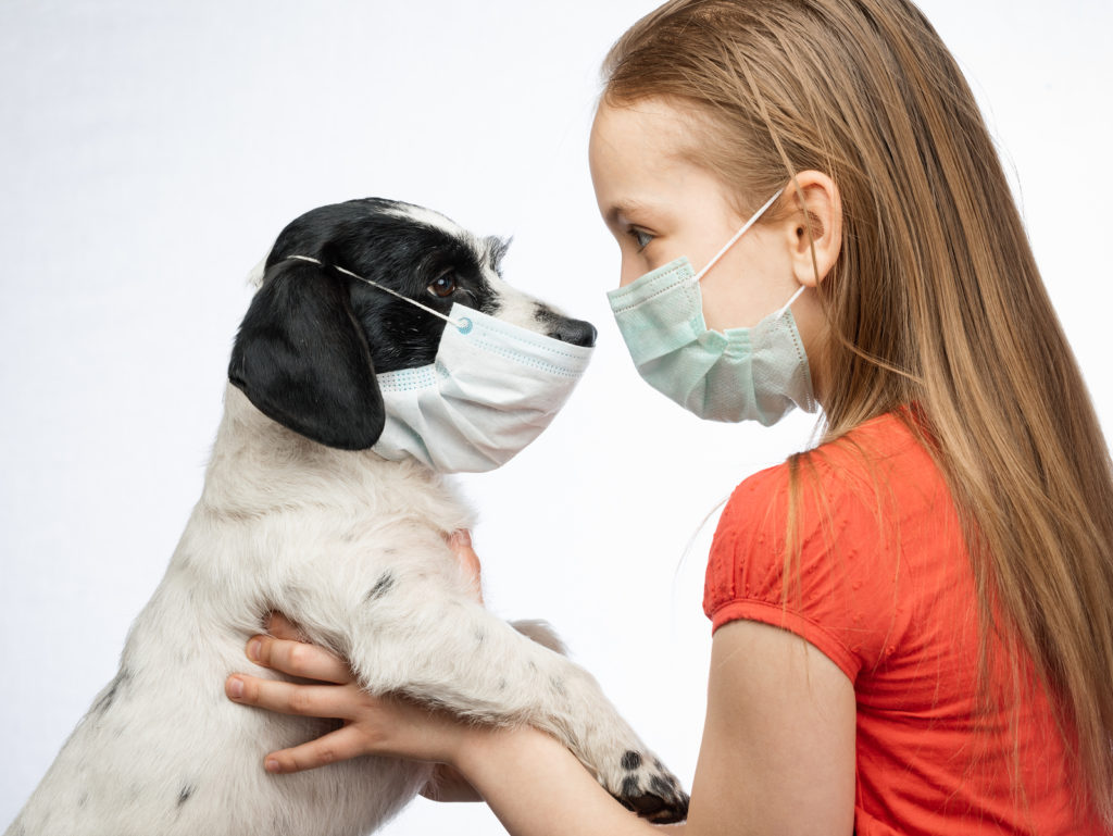 Girl in mask holding puppy in mask